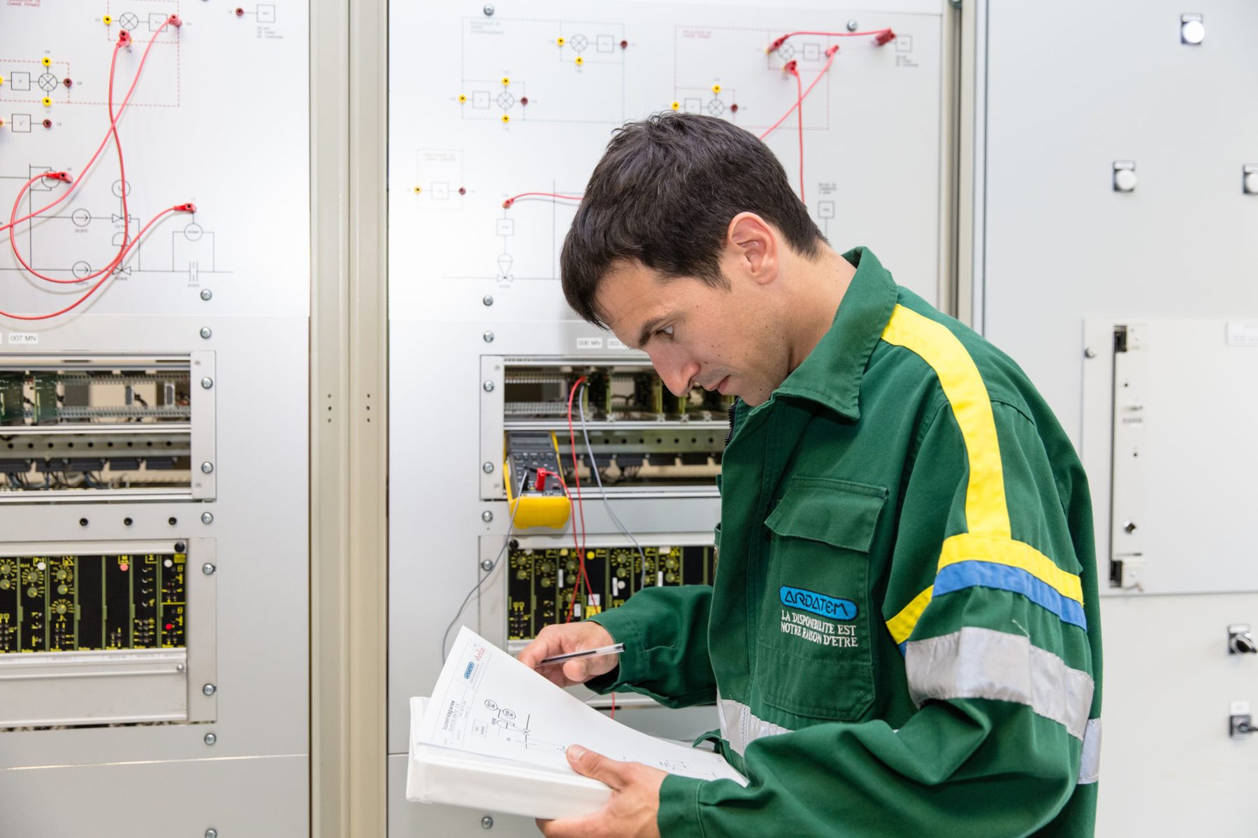 Technicien IDEM vérifiant un schéma devant une armoire électrique